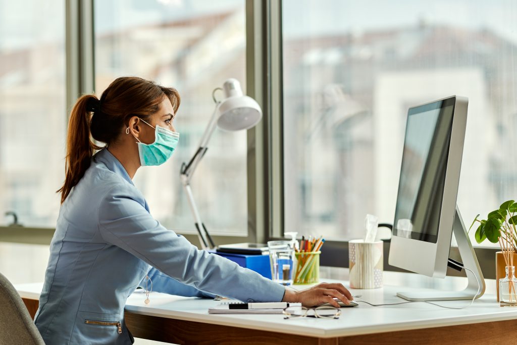 Businesswoman with face mask working on a computer at the office.